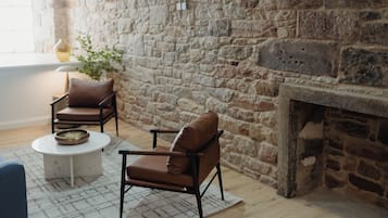 A room with a stone wall, a fireplace, two leather chairs, a small round table, and a blue sofa.