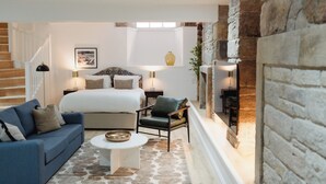 A bedroom with a bed, a blue sofa, a white coffee table, and a stone wall. - Joivy Vaults  (Edinburgh)
