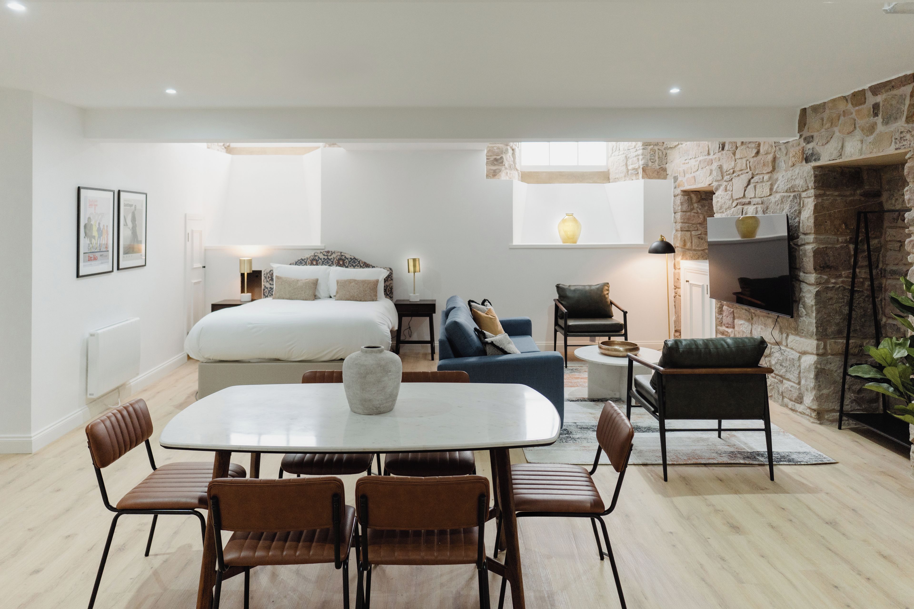 Interior moderno com cama, sofá, mesa de jantar, cadeiras e parede de pedra.