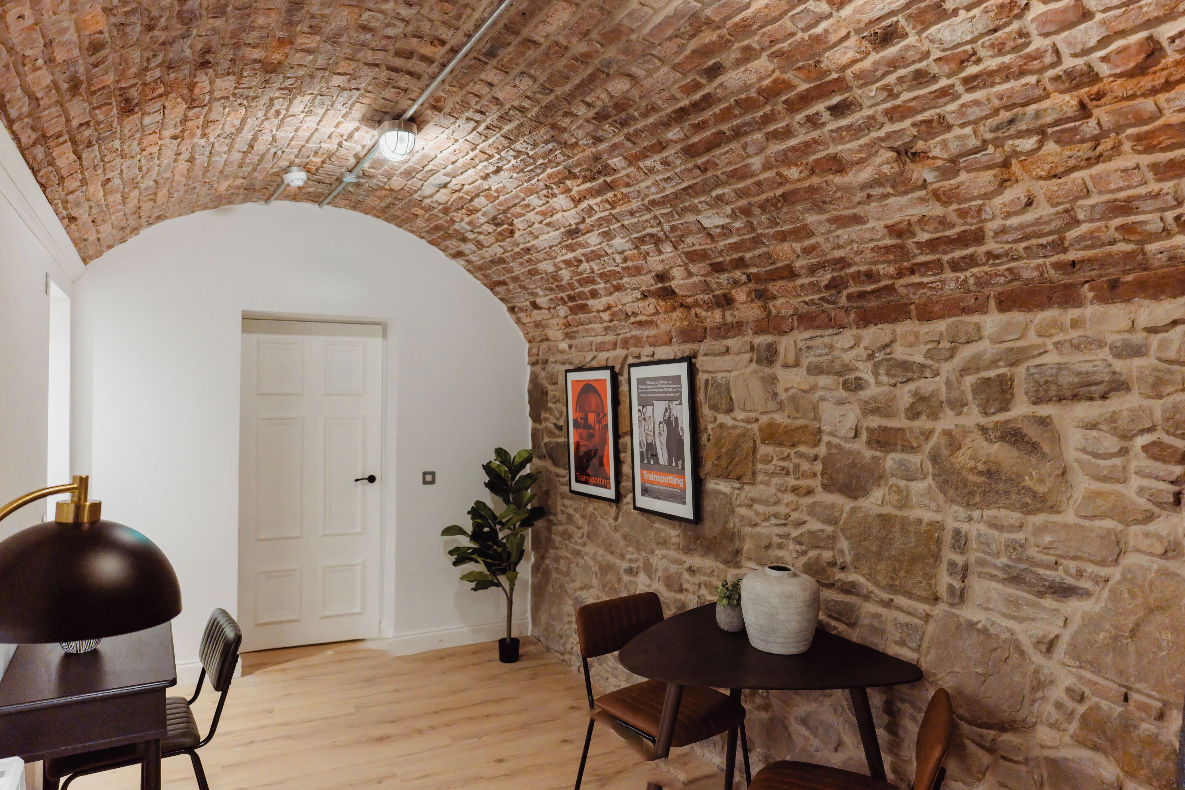A room with a stone wall, a white door, a table with chairs, and a potted plant.