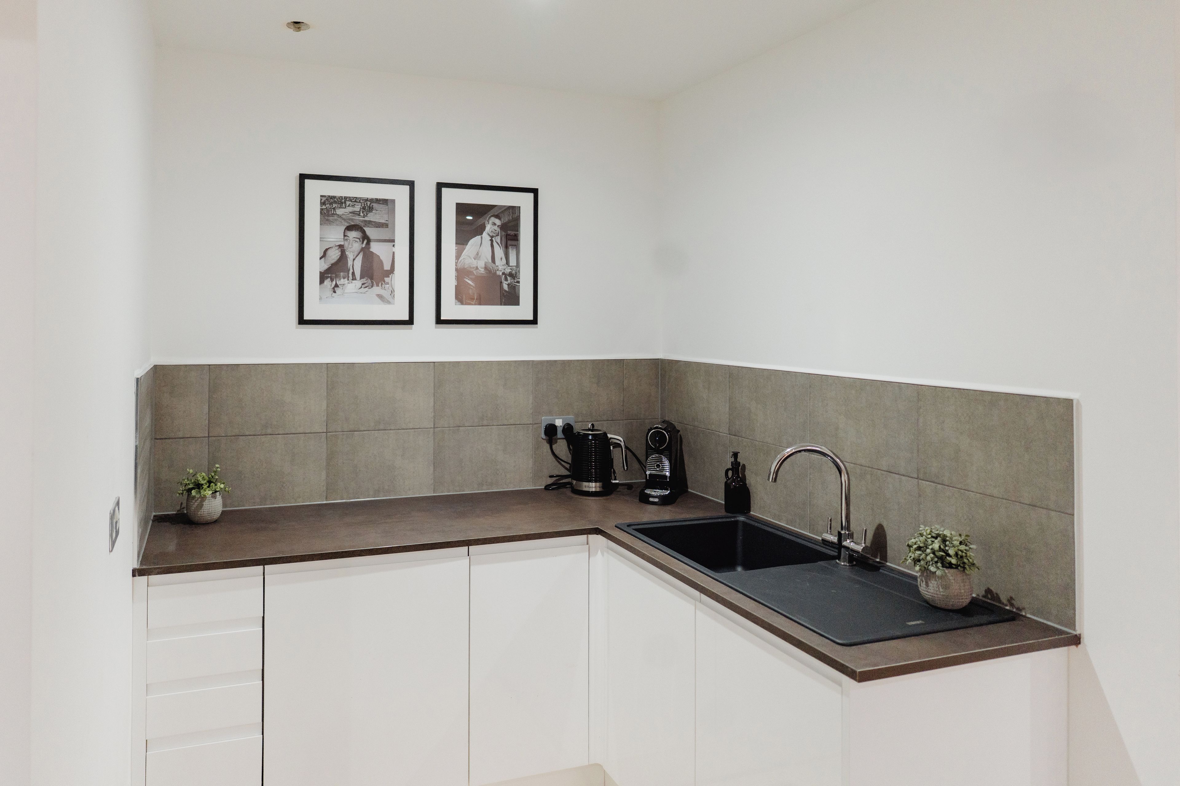 A kitchen with a sink, a coffee maker, and two framed pictures on the wall.