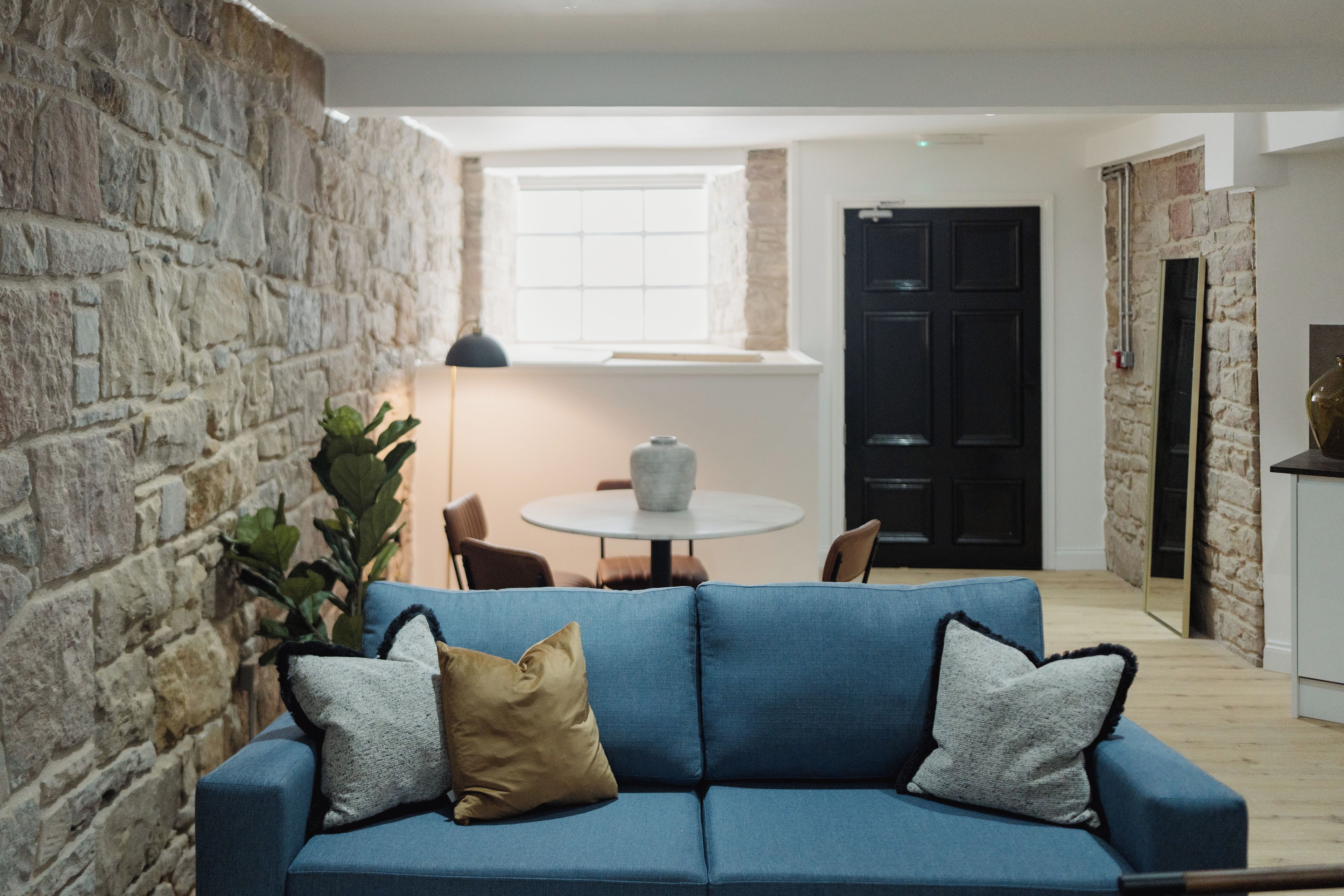A modern living room with a stone wall, a blue sofa with cushions, a round table, and a door in the background.