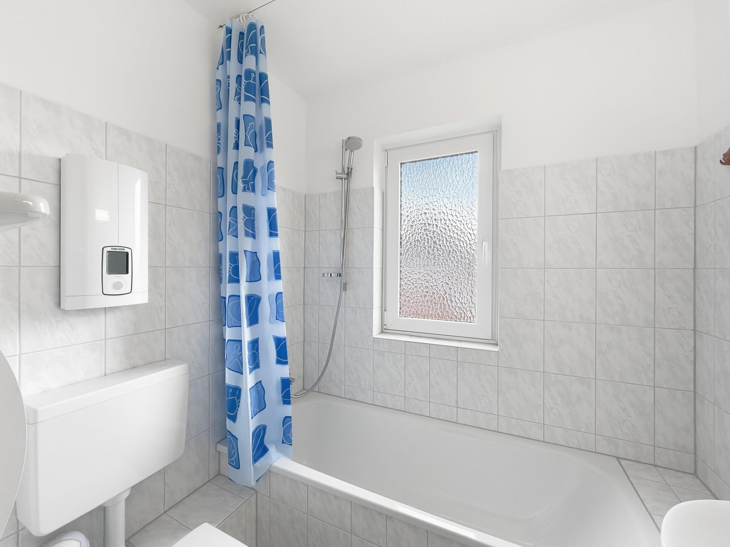 Ein modernes Badezimmer mit einer Badewanne, einer Dusche und einer Toilette. Es gibt ein Milchglasfenster und einen weißen, wandmontierten Seifenspender.