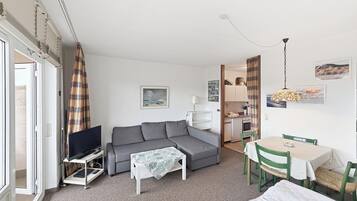 Ein kompakter Wohnbereich mit Sofa, kleinem Tisch, Fernseher und Küchenzeile.