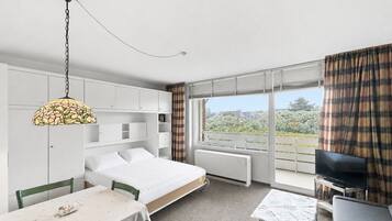 Ein modernes Hotelzimmer mit einem Bett, einem Esstisch, einem Fernseher und einem großen Fenster mit Vorhängen.