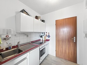 Une cuisine compacte avec des meubles blancs, un évier en acier inoxydable et une porte en bois.
