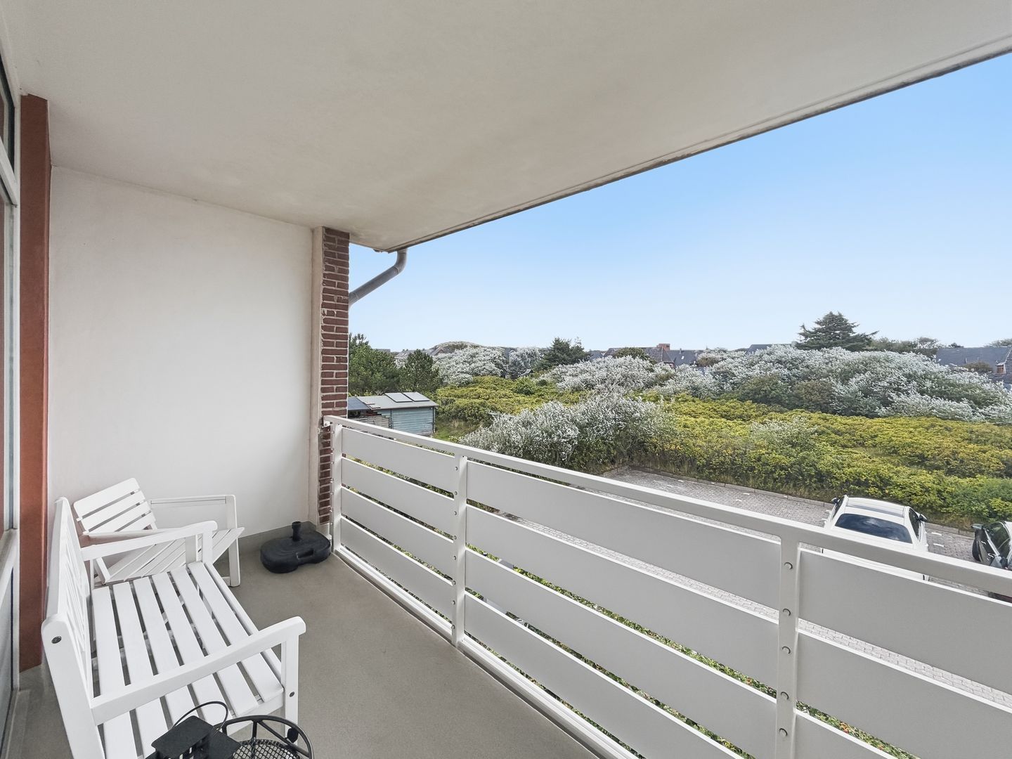 Ein Balkon mit weißen Geländern, einem weißen Stuhl und einem schwarzen Gegenstand auf dem Boden.