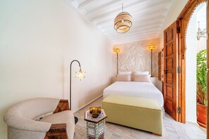 Une chambre à coucher comprenant un lit, une chaise, une table de chevet et une lampe fixée au mur.