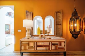 Ein Zimmer mit einem Holzkonsolentisch, einer weißen Lampe und einem Spiegel, der eine gelbe Vase und ein Fenster mit Blickfang zeigt.