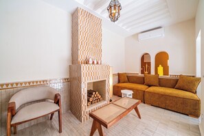 Un salon avec une cheminée à motifs à carreaux, un canapé, un fauteuil et une table.
