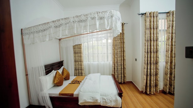Ein Schlafzimmer mit Baldachinbett, Holzboden und Vorhängen an den Fenstern.