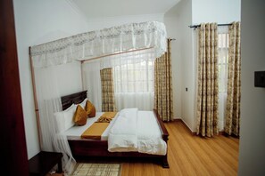 A bedroom with a canopy bed, a wooden floor, and curtains.