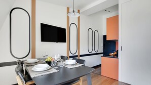 A modern dining area with a black table, white plates, and a flat-screen TV mounted on the wall. - One-Bedroom Superior Apartment (Paris)