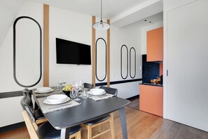 A modern dining area with a black table, white plates, and a flat-screen TV mounted on the wall. - One-Bedroom Superior Apartment (Paris)