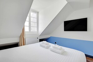 Une chambre avec un lit, une fenêtre, un radiateur et un téléviseur fixé au mur.