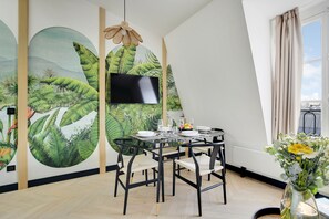 A dining area with a round table, chairs, and a flat-screen TV mounted on the wall. - One-Bedroom Superior Apartment (Paris)