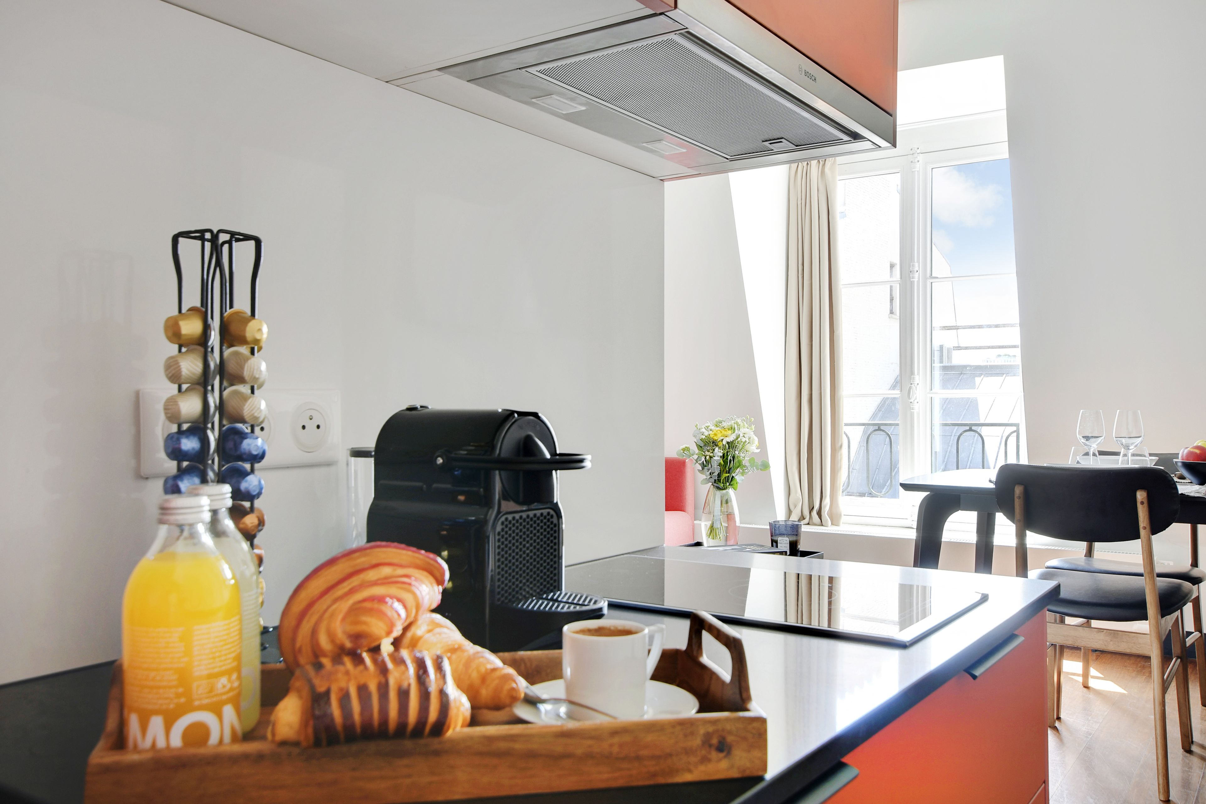 Cozinha moderna com máquina de café, garrafa de suco de laranja e croissants na bancada.