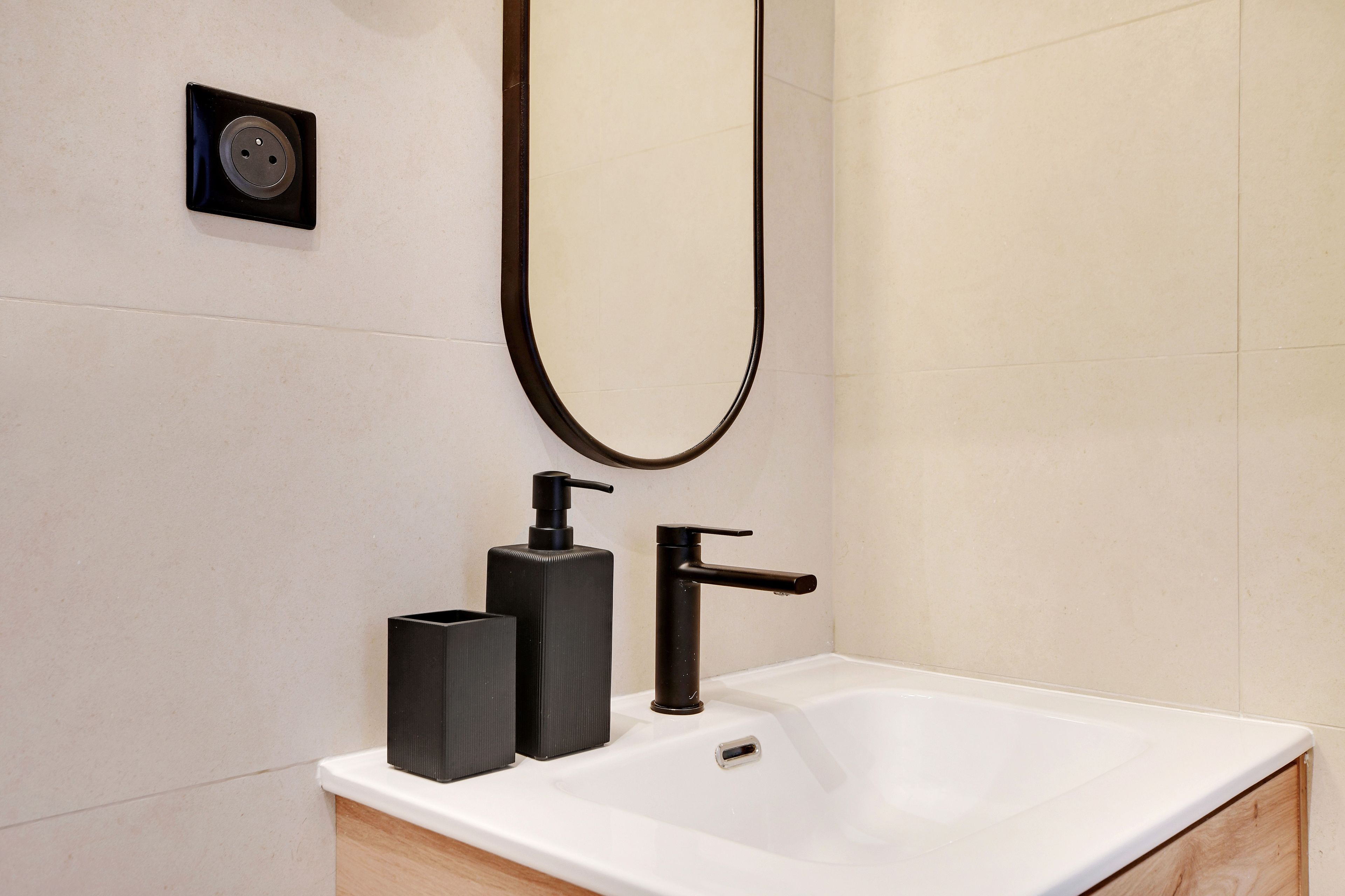 A bathroom with a white sink, black soap dispenser, and faucet.