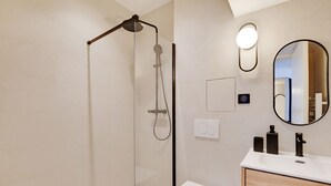 A modern bathroom with a glass-enclosed shower, a white toilet, a wooden vanity with a mirror, and a wall-mounted light fixture. - One-Bedroom Superior Apartment (Paris)