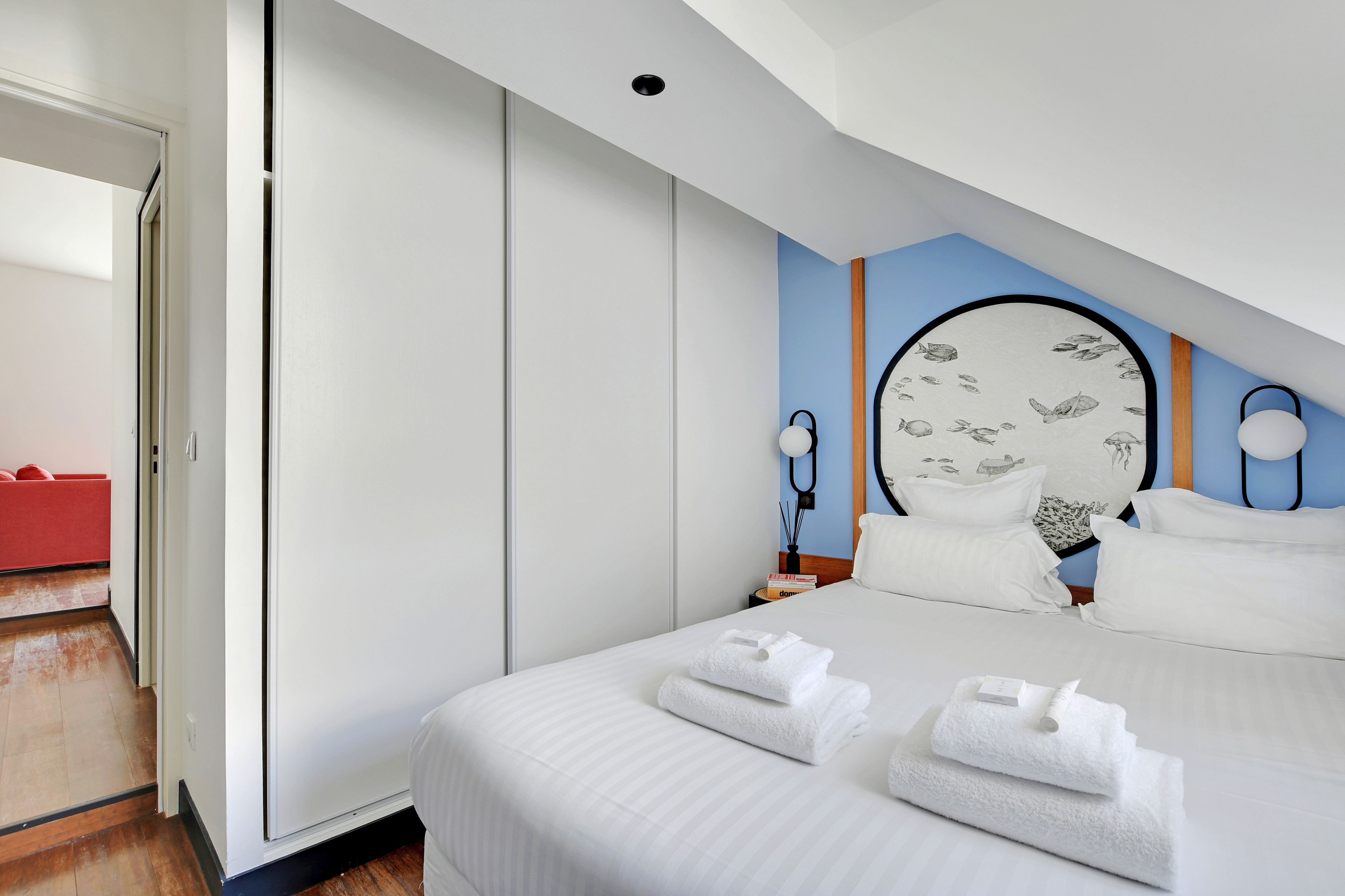 A hotel room with a bed, a nightstand, a red chair, and a door leading to another room.