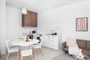 Een moderne keuken met witte kasten, een eettafel met stoelen, een koffieapparaat en een magnetron.