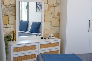 Ein Schlafzimmer mit Steinwand, einem Bett mit blauer Bettwäsche, einer Kommode mit Schubladen und einem Spiegel, der das Bett reflektiert.