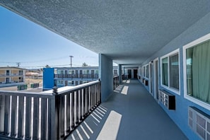 Corredor com varanda de um lado, com guarda-corrimão de metal e fachada azul.