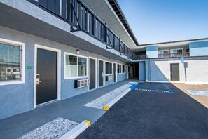 A building with a series of doors and windows, a parking area with handicapped parking spaces, and a clear sky. - 2 Queen Beds | Suite, Non-Smoking, Micfridge (Ridgecrest CA)