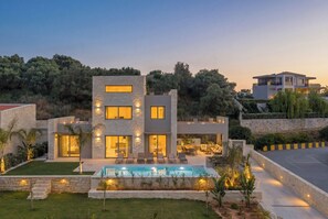 Une maison moderne à deux étages, dotée d’une piscine, d’une façade en pierre et d’un espace extérieur aménagé pour se détendre.