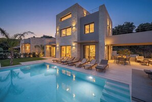 Une maison moderne à deux étages, dotée d’une piscine, d’un espace de détente extérieur et de murs en pierre.