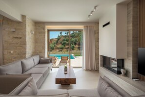 A modern living room with a stone wall, a sofa, a coffee table, and a TV. - Villa Agapi is the largest residence of the La Divina Luxury Villas collection (Chania)