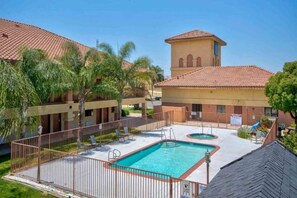 A hotel with a swimming pool, palm trees, and a building with a tiled roof. - 1 King Bed | Non-Smoking (Santa Nella)