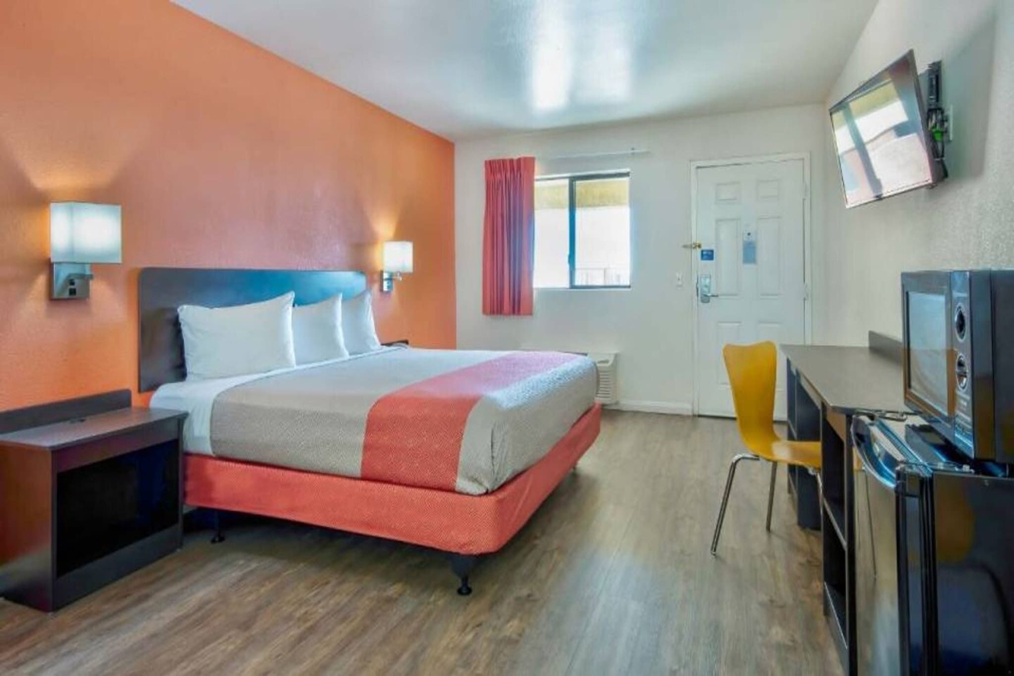 Ein Hotelzimmer mit einem Bett, einem Schreibtisch mit Stuhl, einem Fernseher und einem Fenster mit Vorhängen.