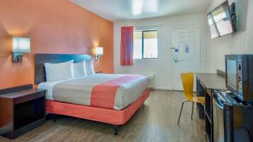 Ein Hotelzimmer mit einem Bett, einem Schreibtisch mit Stuhl, einem Fernseher und einem Fenster mit Vorhängen.
