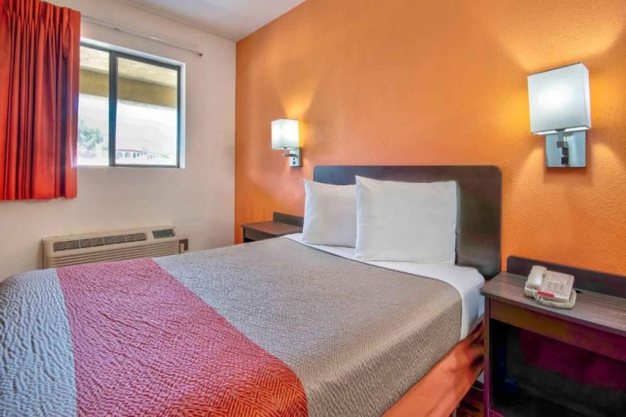 Una habitación de hotel con cama, calefacción, ventana con cortinas y teléfono instalado en la pared.