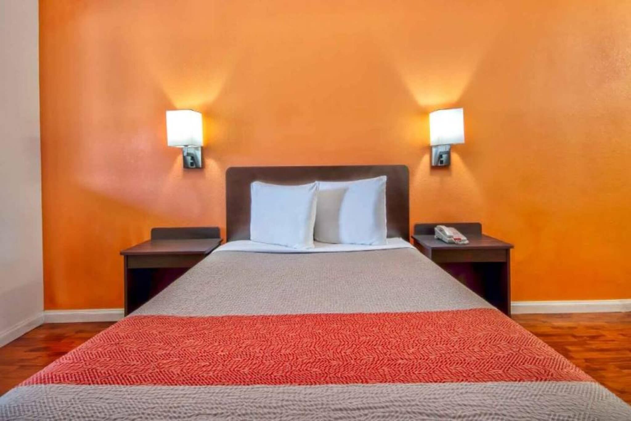 A hotel room with a bed, two bedside tables, and wall-mounted lamps.
