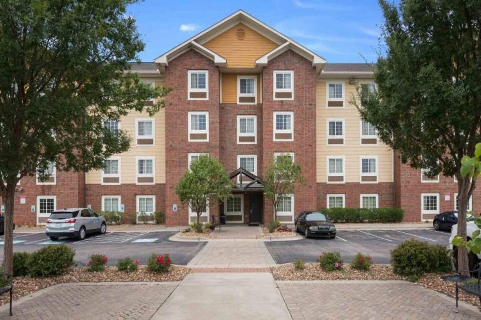 A multi-story hotel with a brick facade, a central entrance, and a parking lot.