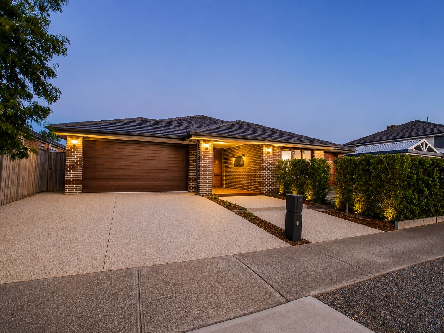 A residential house with a garage, brick exterior, and a well-lit driveway.