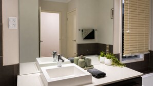 Un baño moderno con dos lavamanos, un espejo, un perchero para toallas y una ventana con persianas.