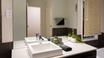 A modern bathroom with two sinks, a mirror, a towel rack, and a window with blinds.