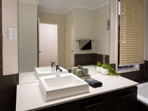 A modern bathroom with two sinks, a mirror, a towel rack, and a window with blinds. - Spacious Bali Retreat | Gaming, Gym & Pool access (Tarneit)