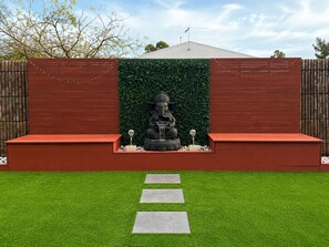 Ein Garten mit einer Statue einer Gottheit, einer Hecke und einem Weg.