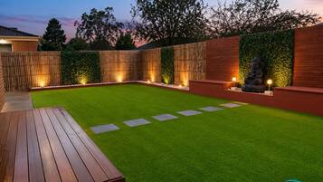 A backyard with artificial grass, a wooden deck, a seating area, and a decorative Buddha statue.