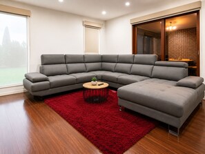 A modern living room with a grey sectional sofa, a small round coffee table, and a red rug. - Spacious Bali Retreat | Gaming, Gym & Pool access (Tarneit)