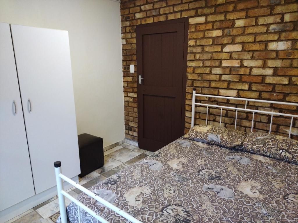 A bedroom with a bed, a wardrobe, a door, and a brick wall.