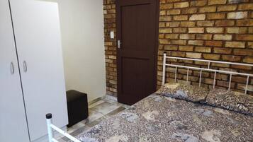 A bedroom with a bed, a wardrobe, a door, and a brick wall.