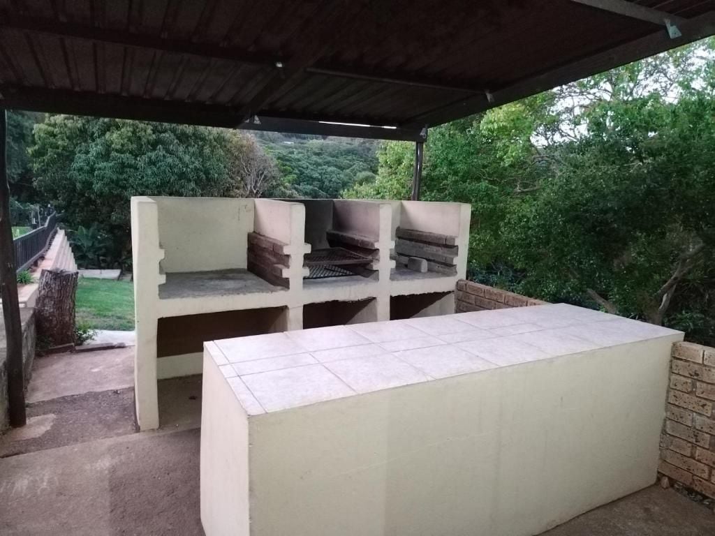 Un área de barbacoa al aire libre con una parrilla empotrada y una superficie plana, rodeada de vegetación.