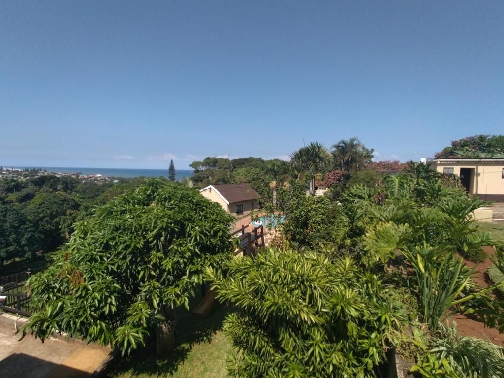 A residential area with lush greenery, a clear sky, and a view of the sea in the distance.