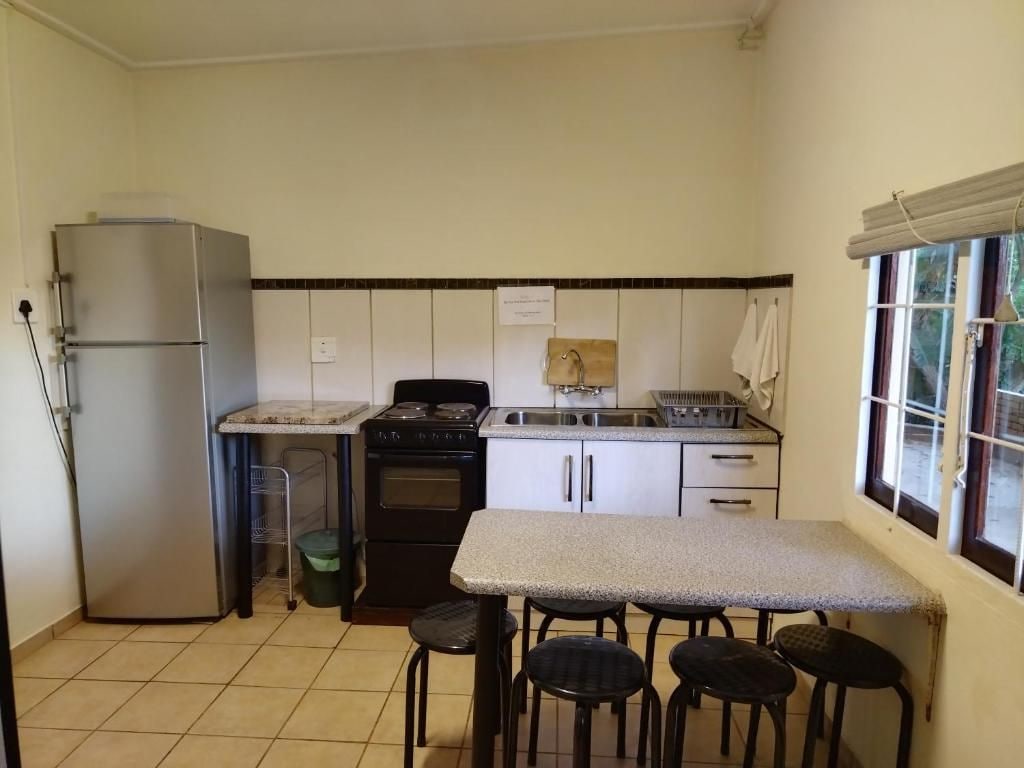 A compact kitchen with a refrigerator, stove, sink, and a small dining table with stools.