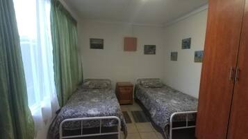 A room with two single beds, a wooden wardrobe, and a small bedside table.